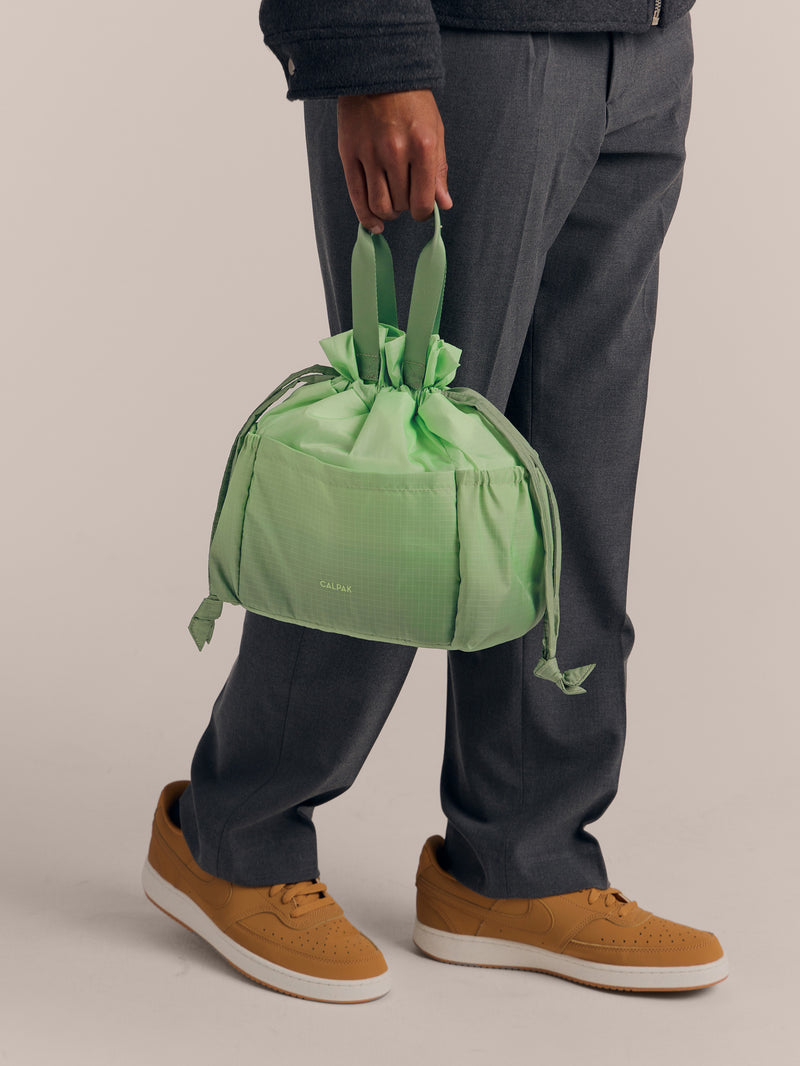 Model holding the handles of CALPAK Insulated Lunch Bag in ombre green Matcha