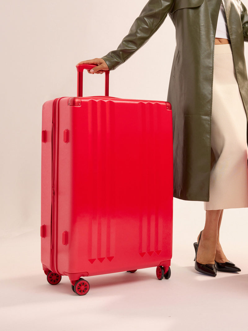 Model standing besides CALPAK Ambeur Large Luggage in metallic red