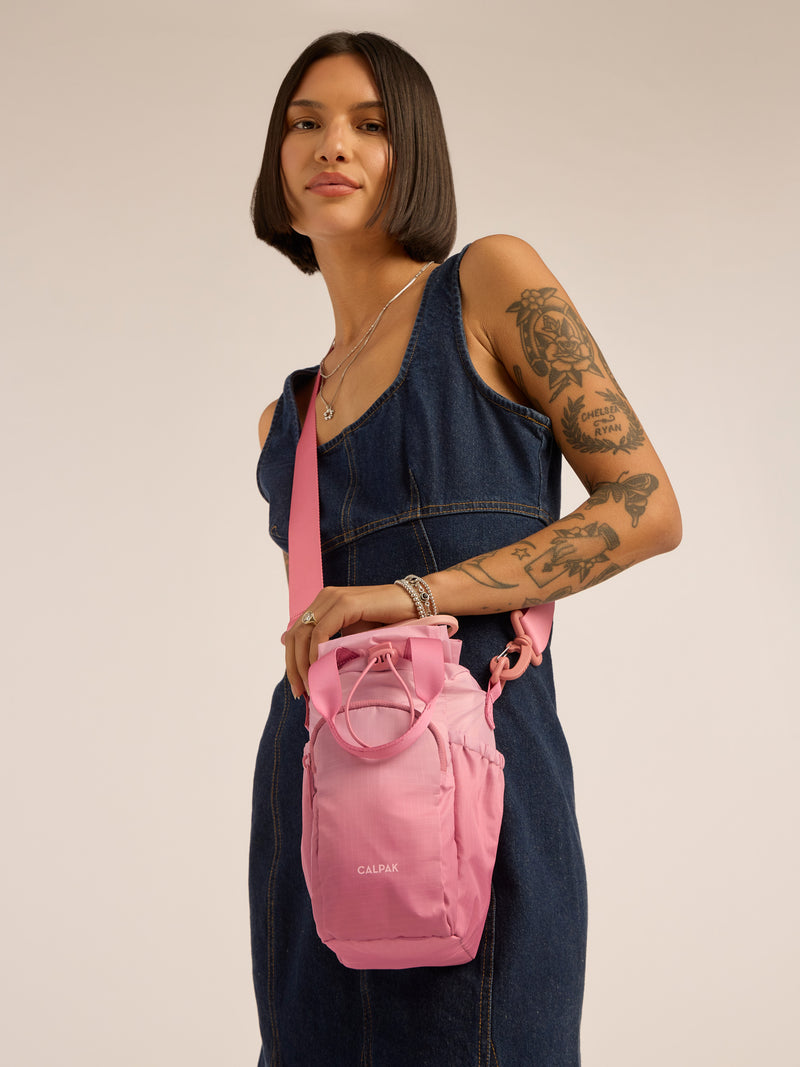 Model wearing pink shoulder strap of CALPAK Water Bottle Holder in pink ombre Tea Rose