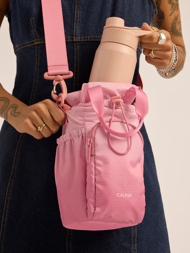 Model inserting water bottle into the CALPAK Water Bottle Holder in pink ombre Tea Rose