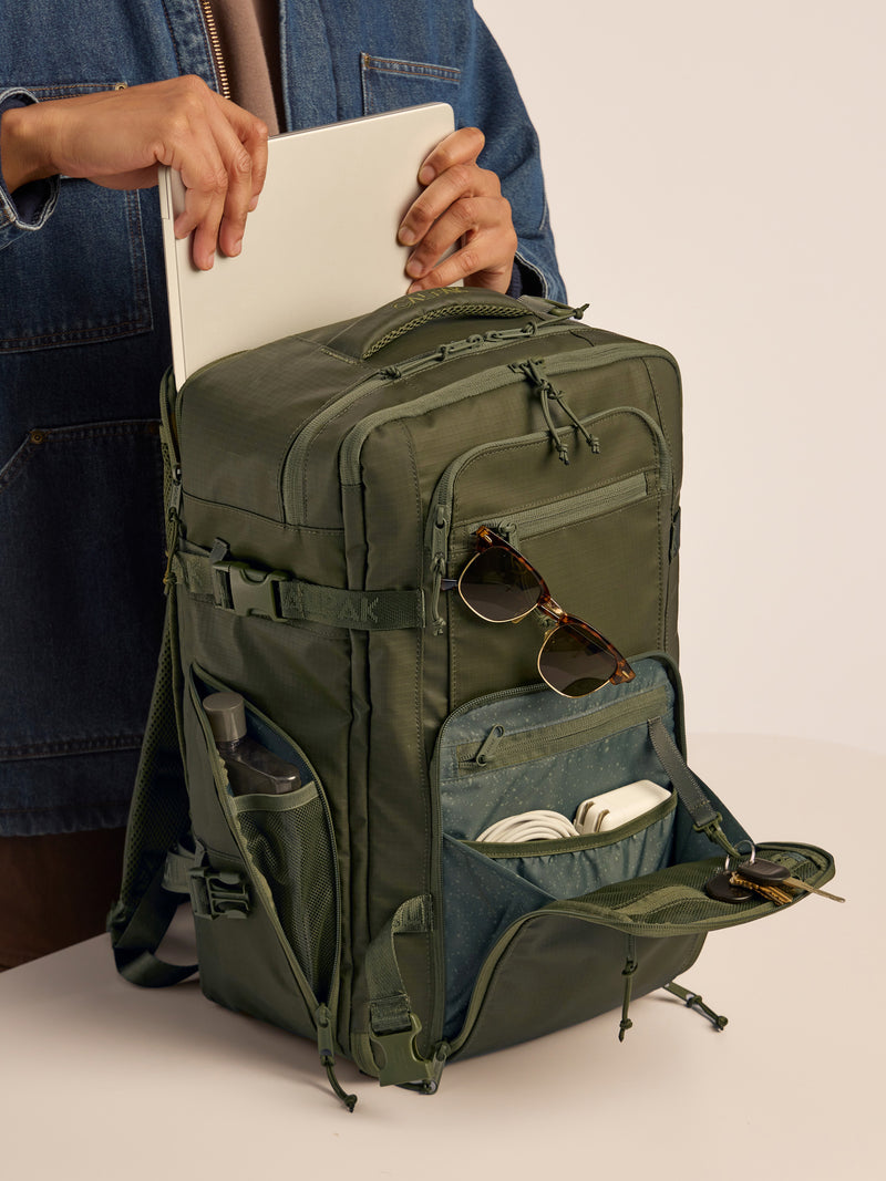 Model putting in laptop into the CALPAK Terra 26L Laptop Backpack Duffel in dark green Matte Pine duffel