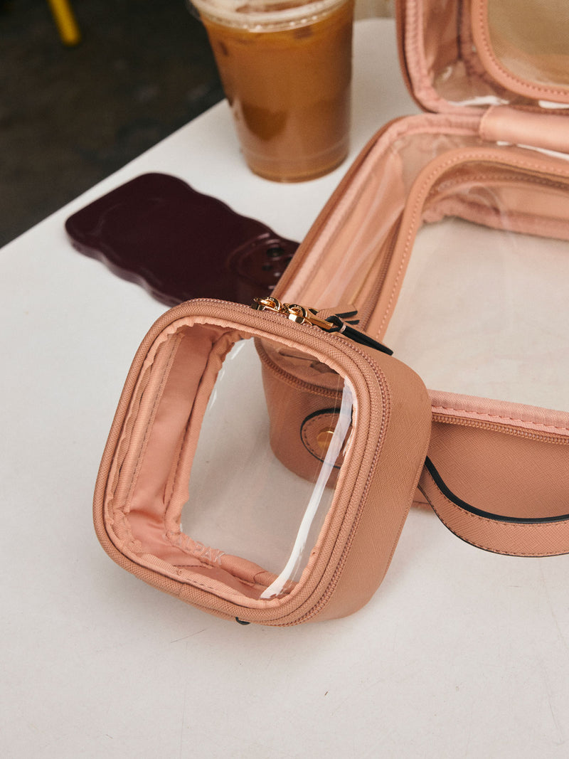 CALPAK Tiny Clear Cosmetic Case in light brown Caramel on a white table with other CALPAK clear cosmetic case, coffee, and a phone  in the background