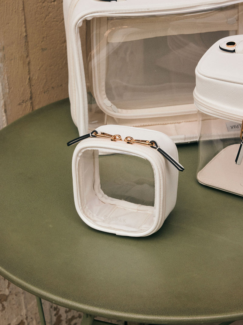 CALPAK Tiny Clear Cosmetic Case in White on a green table with other CALPAK clear cosmetic cases in the background