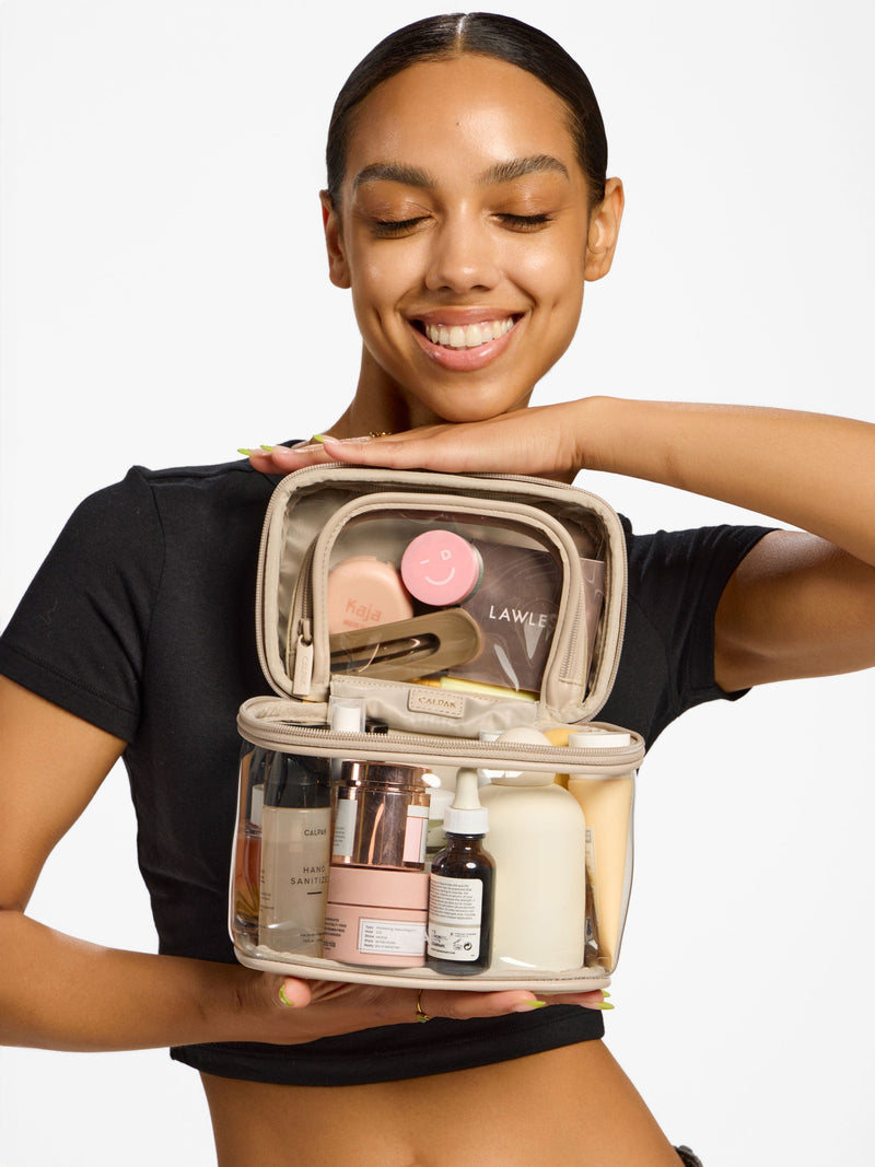 Model holding CALPAK Clear Train Case makeup bag in stone