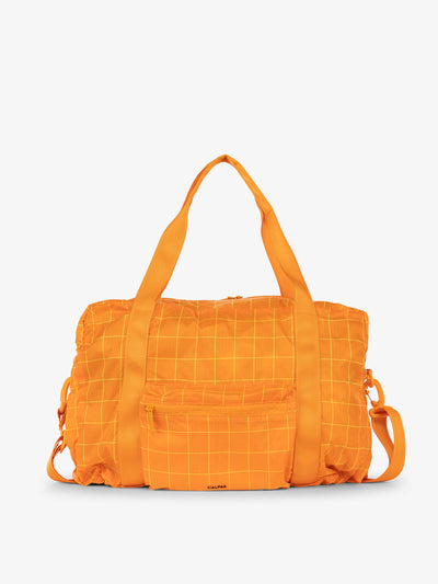 CALPAK Compakt duffel bag with removable crossbody strap and water resistant fabric in orange grid; KDB2001-ORANGE-GRID