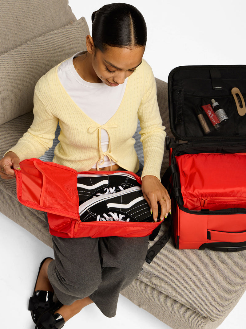 Model placing shoes within red CALPAK Compakt Shoe Bag