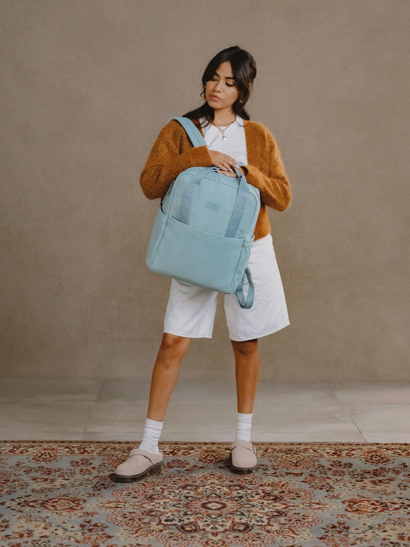 Model wearing strap of CALPAK Connect Laptop Backpack over shoulder in bluebell blue