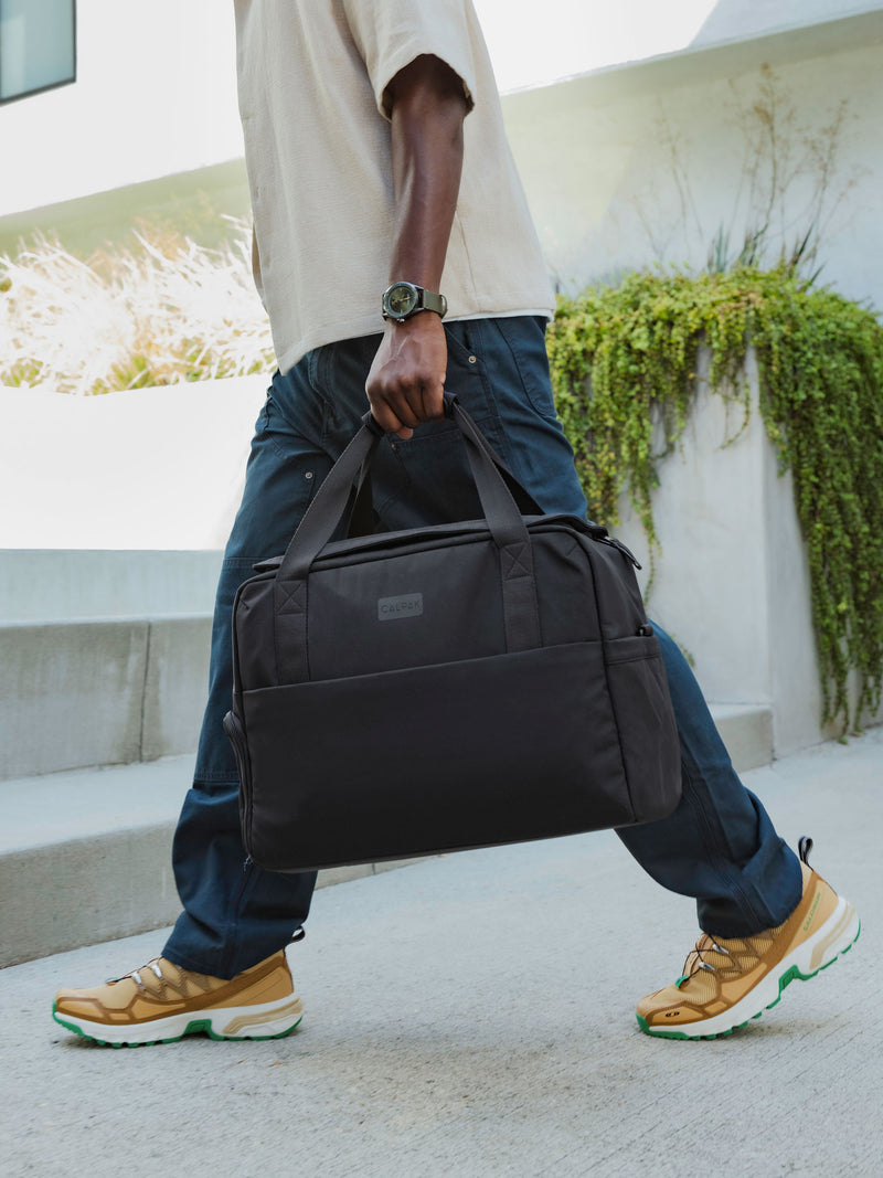 Model holding CALPAK Connect Laptop Duffel by durable carrying handles in black