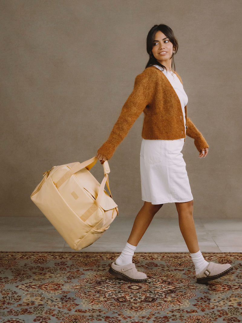 Model walking and holding CALPAK Connect Laptop Duffel in sunshine yellow