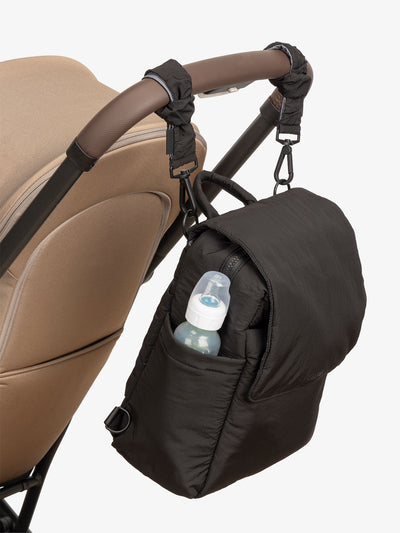 CALPAK Convertible Mini Diaper Backpack attached to stroller by CALPAK Stroller Straps in black; BBPC2401-BLACK, BPC2401-BLACK
