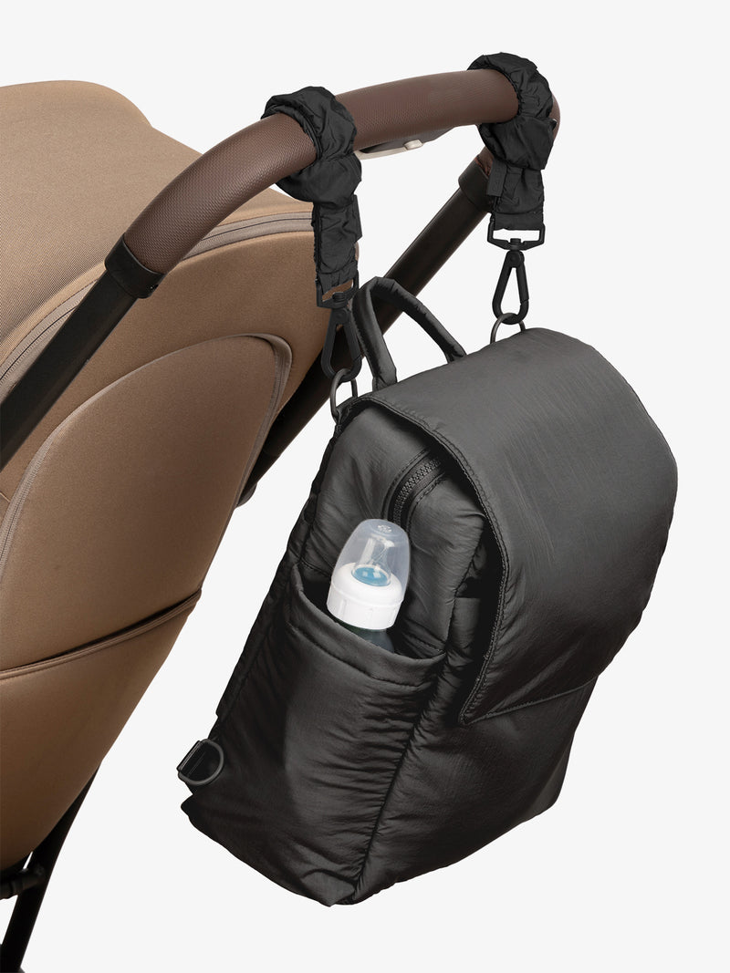 CALPAK Convertible Mini Diaper Backpack in Black with Black Stroller Straps attached to a brown stroller