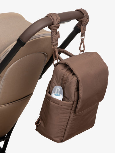 CALPAK Convertible Mini Diaper Backpack attached to stroller by CALPAK Stroller Straps in hazelnut brown; BBPC2401-HAZELNUT, BPC2401-HAZELNUT