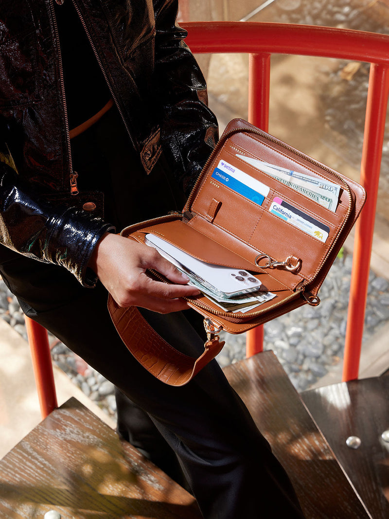 Model displaying interior of CALPAK Croc Wallet featuring multiple pockets for cards, travel documents, and cellphone in brown cognac