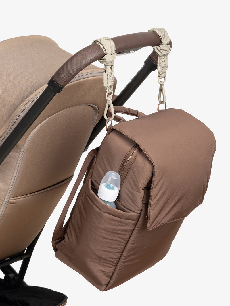 CALPAK Diaper Backpack in brown Hazelnut with white Oatmeal Stroller Straps attached to a brown stroller