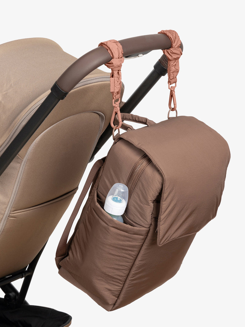 CALPAK Diaper Backpack in brown Hazelnut with pink Peony Stroller Straps attached to a brown stroller