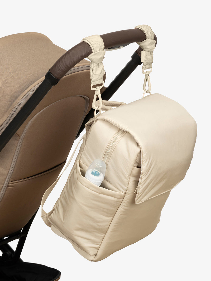 CALPAK Diaper Backpack in white Oatmeal with white Oatmeal Stroller Straps attached to a brown stroller