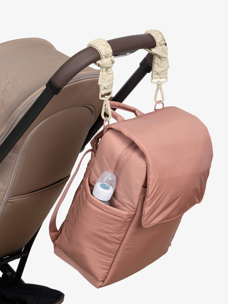 CALPAK Diaper Backpack in pink Peony with white Oatmeal Stroller Straps attached to a brown stroller