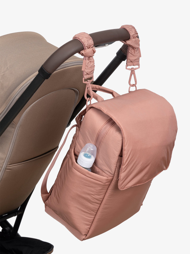 CALPAK Diaper Backpack in pink Peony with pink Peony Stroller Straps attached to a brown stroller