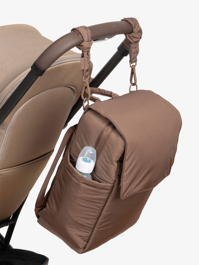 CALPAK Diaper Backpack with Laptop Sleeve attached to stroller by CALPAK Stroller Straps in hazelnut; BPB2401-HAZELNUT, BBPB2401-HAZELNUT view 1