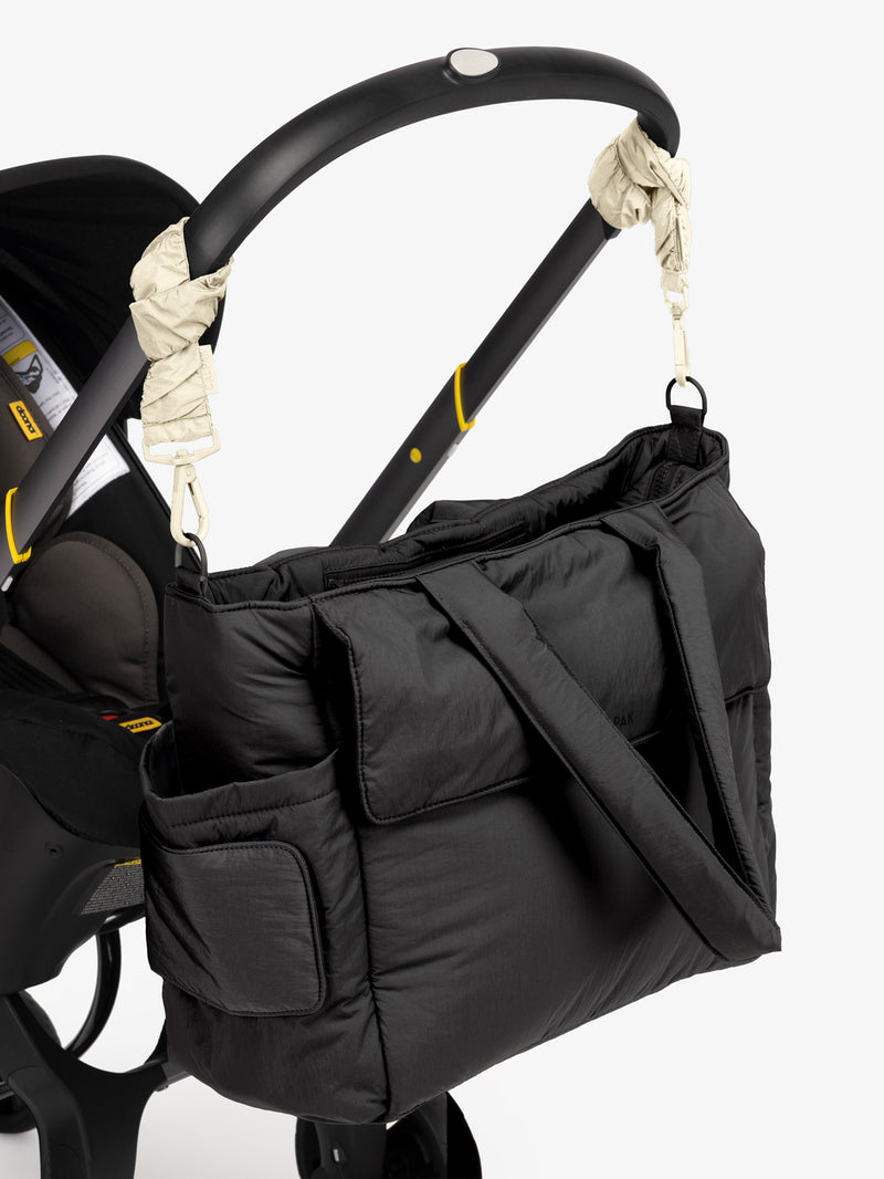 CALPAK Diaper Tote Bag in Black with white Oatmeal Stroller Straps attached to a black stroller