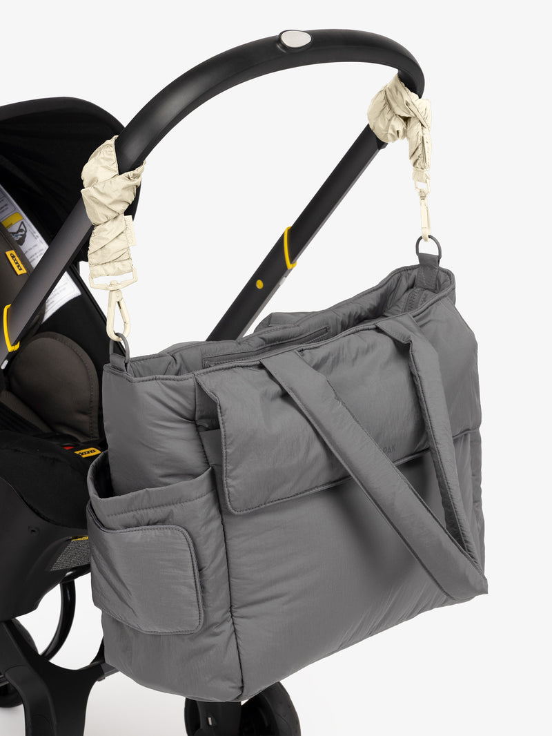 CALPAK Diaper Tote Bag in grey Slate with white Oatmeal Stroller Straps attached to a black stroller