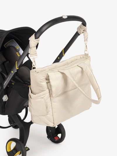 CALPAK Diaper Tote Bag with Stroller Straps attached to stroller handle in oatmeal beige