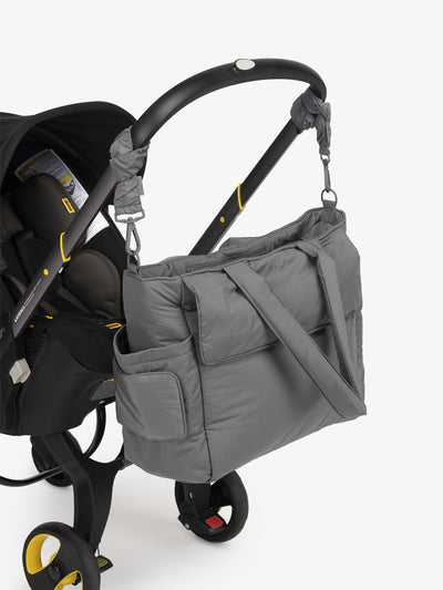 CALPAK Diaper Tote Bag with Stroller Straps attached to stroller handle in slate gray