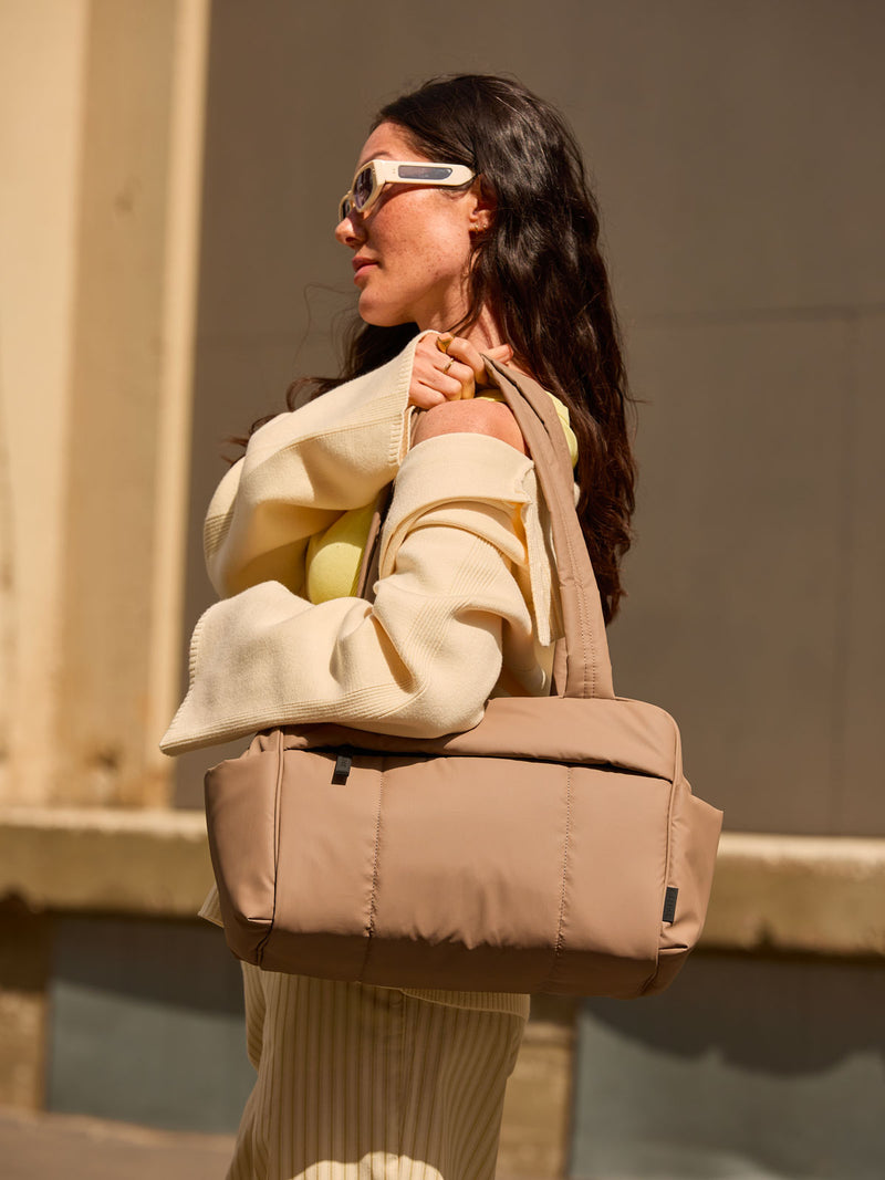 CALPAK Mini Duffel in brown Chocolate  with puffy exterior, interior and exterior pockets, and padded shoulder straps being worn by a model