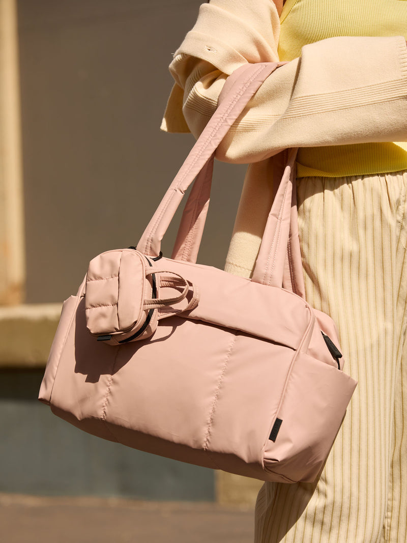 CALPAK Mini Duffel in pink Rose Quartz with puffy exterior, interior and exterior pockets, and padded shoulder straps being worn by a model