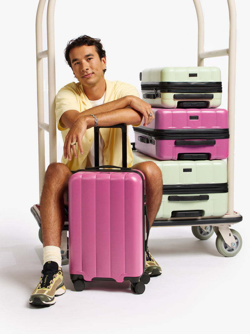 Model resting arms on adjustable handle of CALPAK Evry Carry-On Luggage in pinkish red raspberry