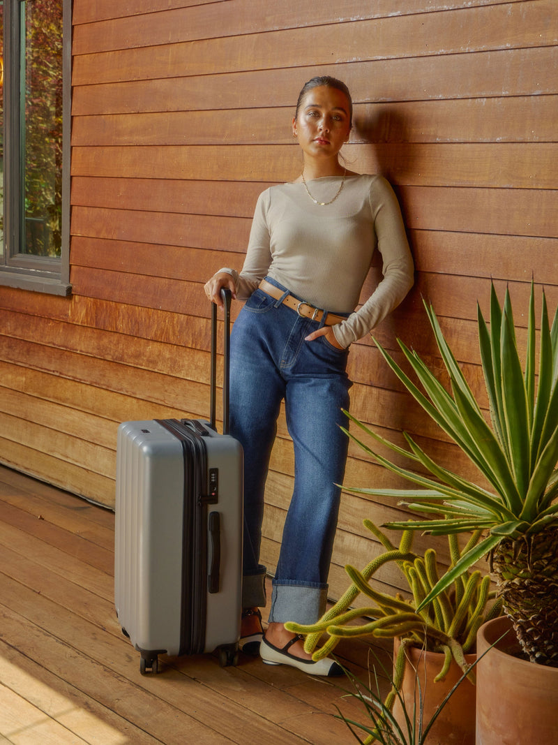 Model standing besides CALPAK Evry Medium Luggage in smoke