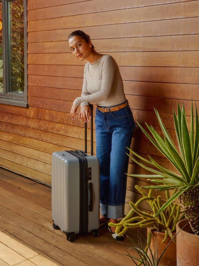 Model leaning over adjustable handle of CALPAK Evry Medium Luggage in smoke gray