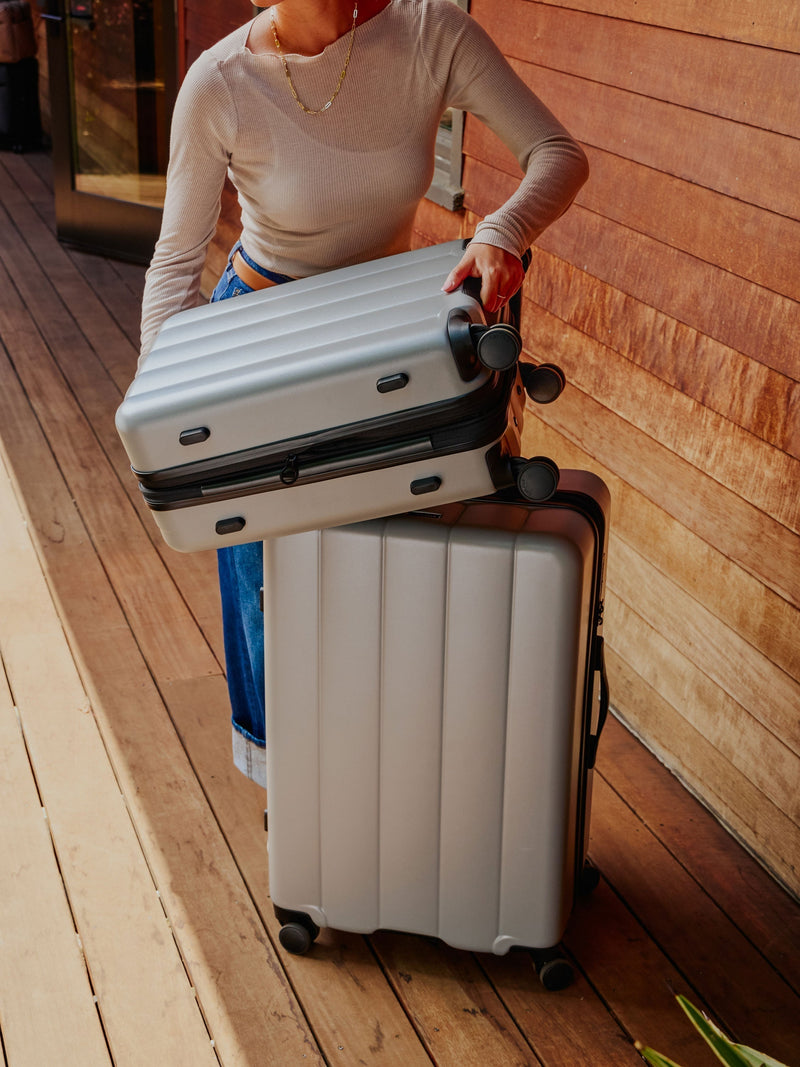 CALPAK Model displaying the Evry carry-on luggage and large luggage in gray smoke