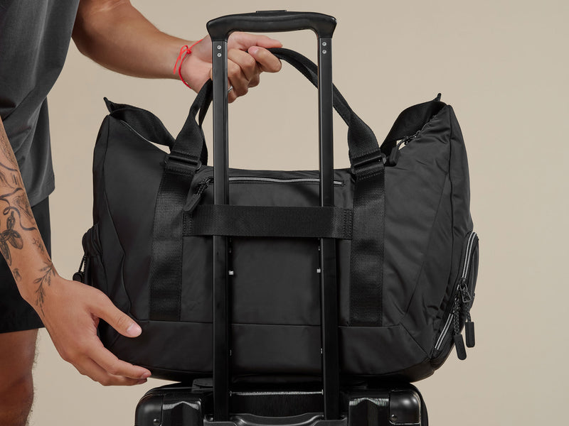 Black Gym bag being placed on Trolley of Carry-on luggage by CALPAK; BTBF2401-BLACK