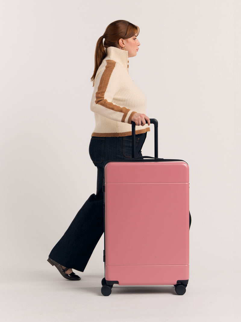 Model with CALPAK Hue large 30 inch hard shell luggage in pink Mauve