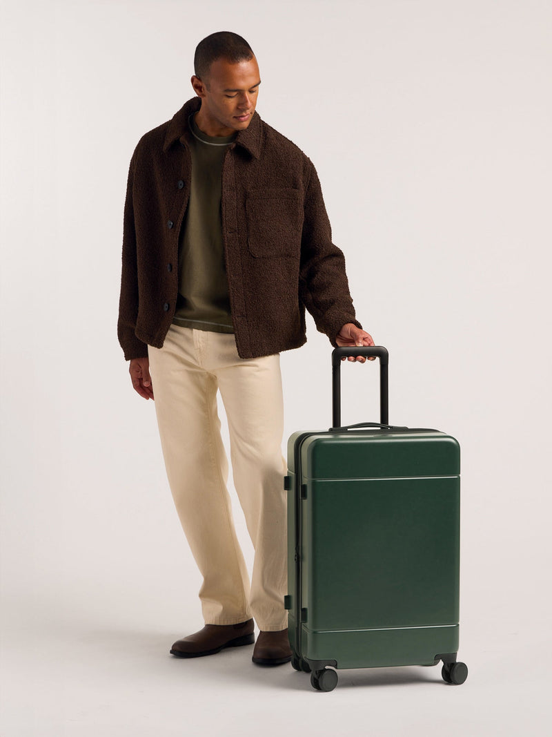 Model holding handle of the CALPAK Hue Medium & Large Luggage in green Emerald