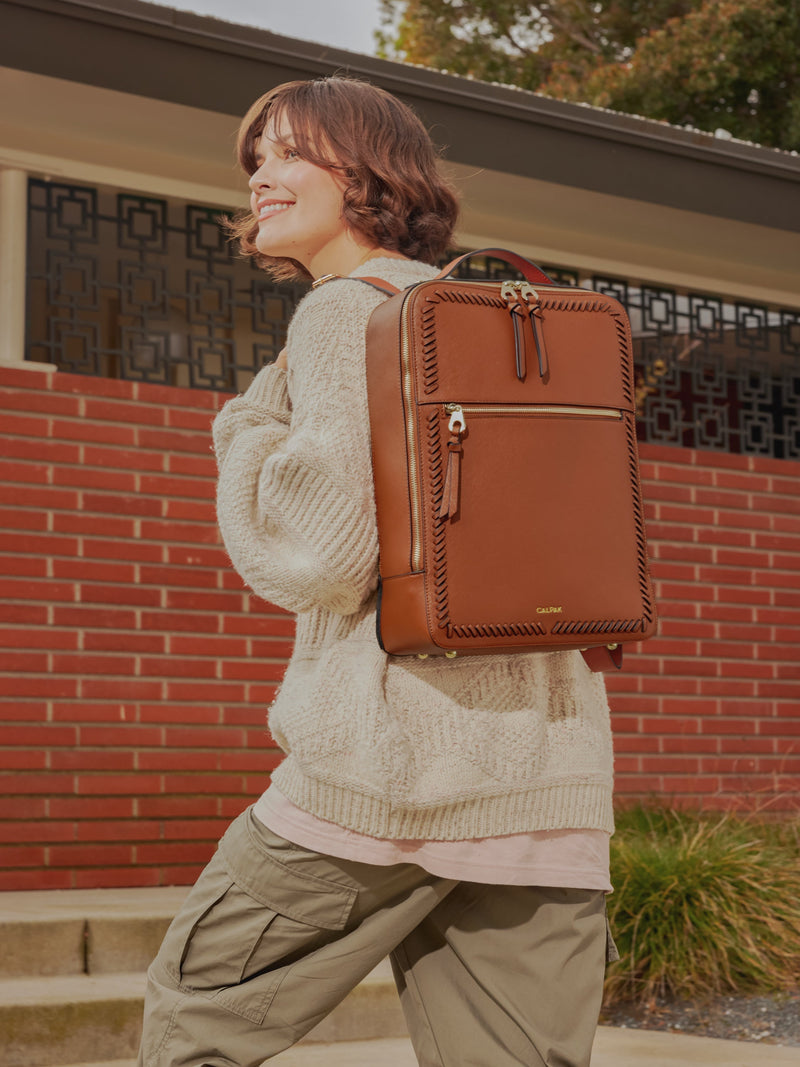 Model carrying CALPAK Kaya Laptop Backpack with adjustable straps and zippered pockets in brown