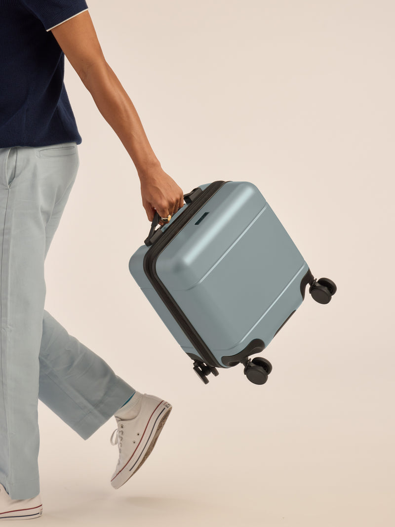 Model carrying the CALPAK Hue Mini Carry-On Luggage in blue Bluebell