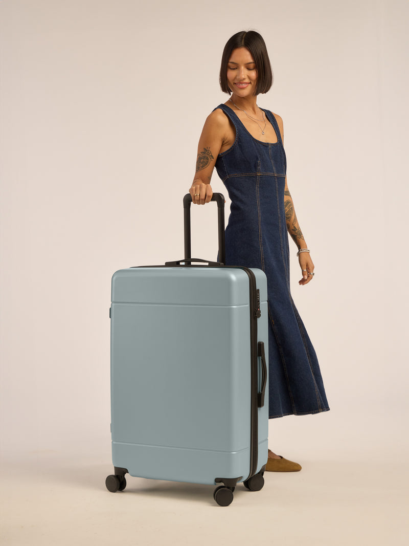 Model with CALPAK Hue Large Luggage in blue Bluebell