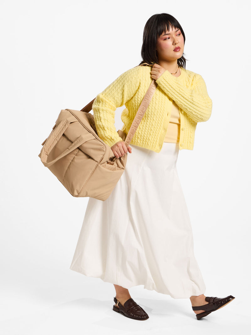 Model using removable strap of CALPAK luka duffel over shoulder in latte