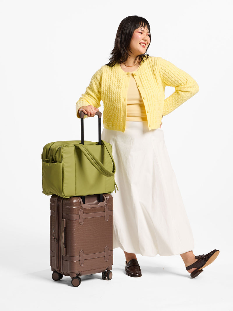 Model displaying luggage trolley sleeve of CALPAK Luka Duffel in pistachio