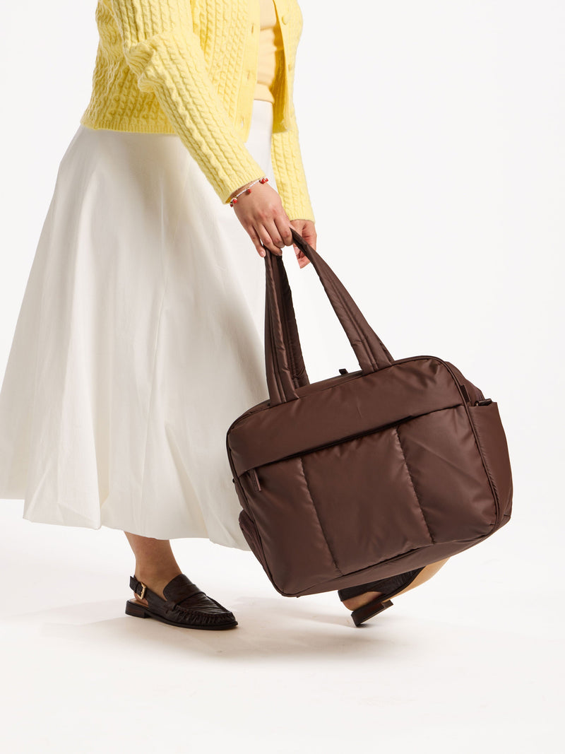 Model holding CALPAK Luka Duffel by handle in dark brown