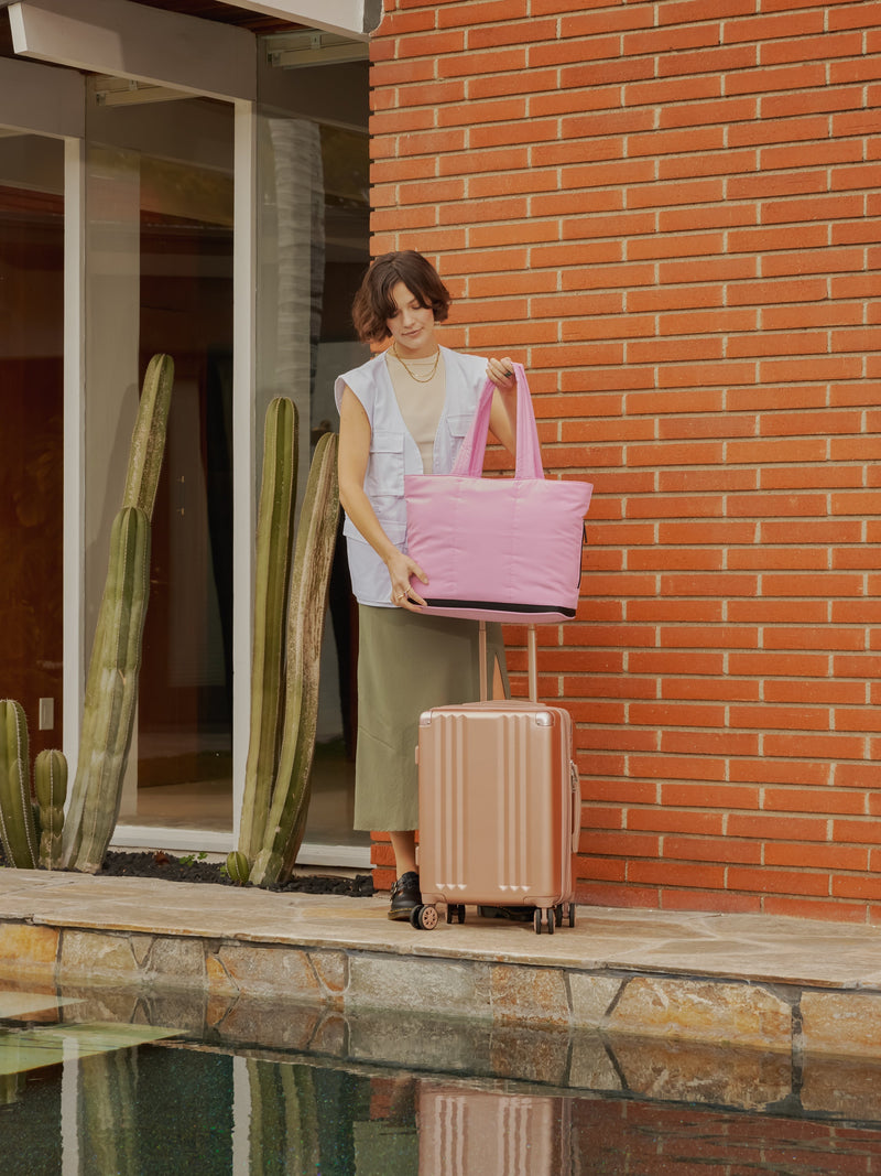 Model placing CALPAK Luka expandable laptop tote bag on carry on with trolley sleeve in bubblegum