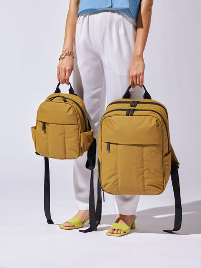 Model holding CALPAK Luka 15 Inch Laptop Backpack and Luka mini backpack with soft puffy exterior in khaki brown