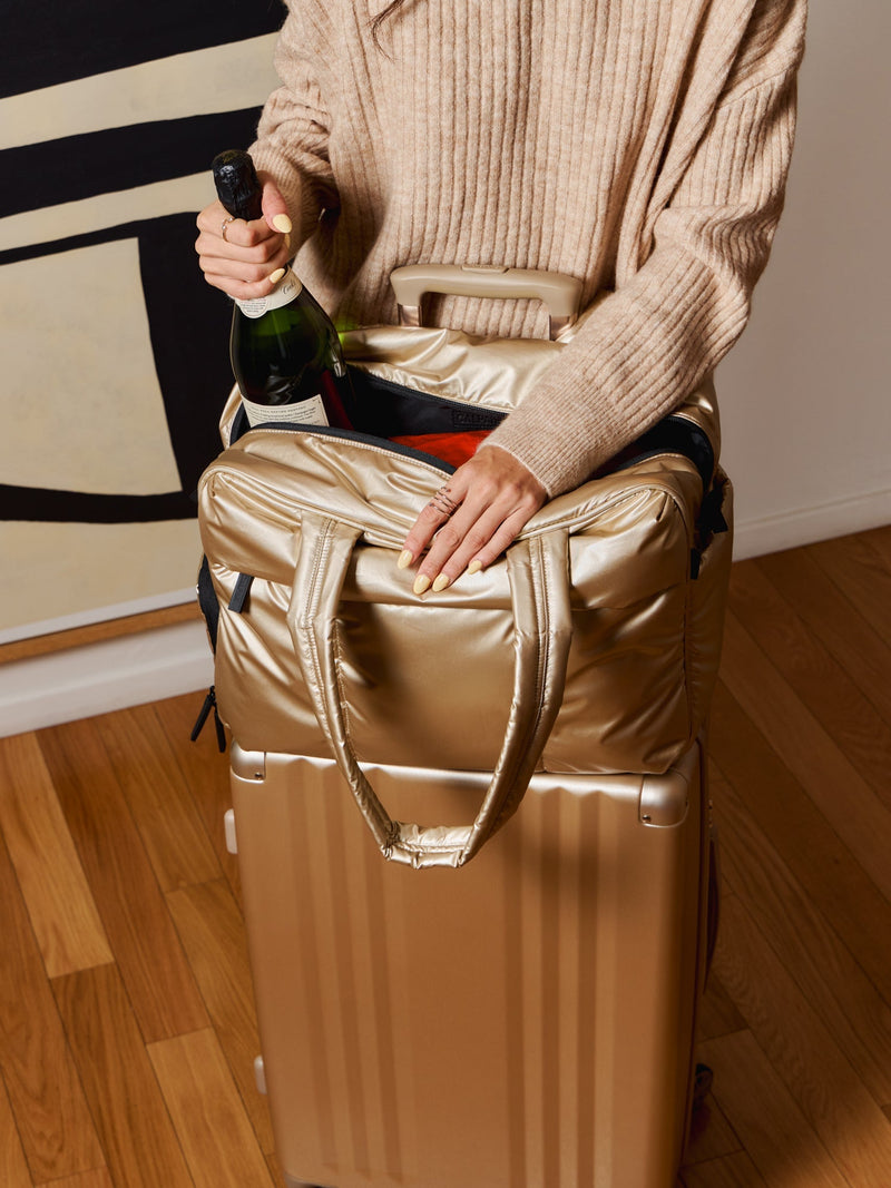 Model resting CALPAK Luka Large Duffel on top of Ambeur Medium Luggage in gold