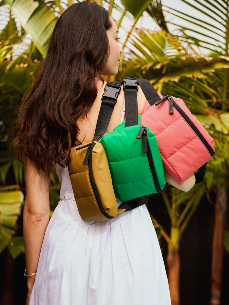 Model carrying CALPAK Luka small Belt Bags with puffy exterior and adjustable straps in khaki, green apple and watermelon