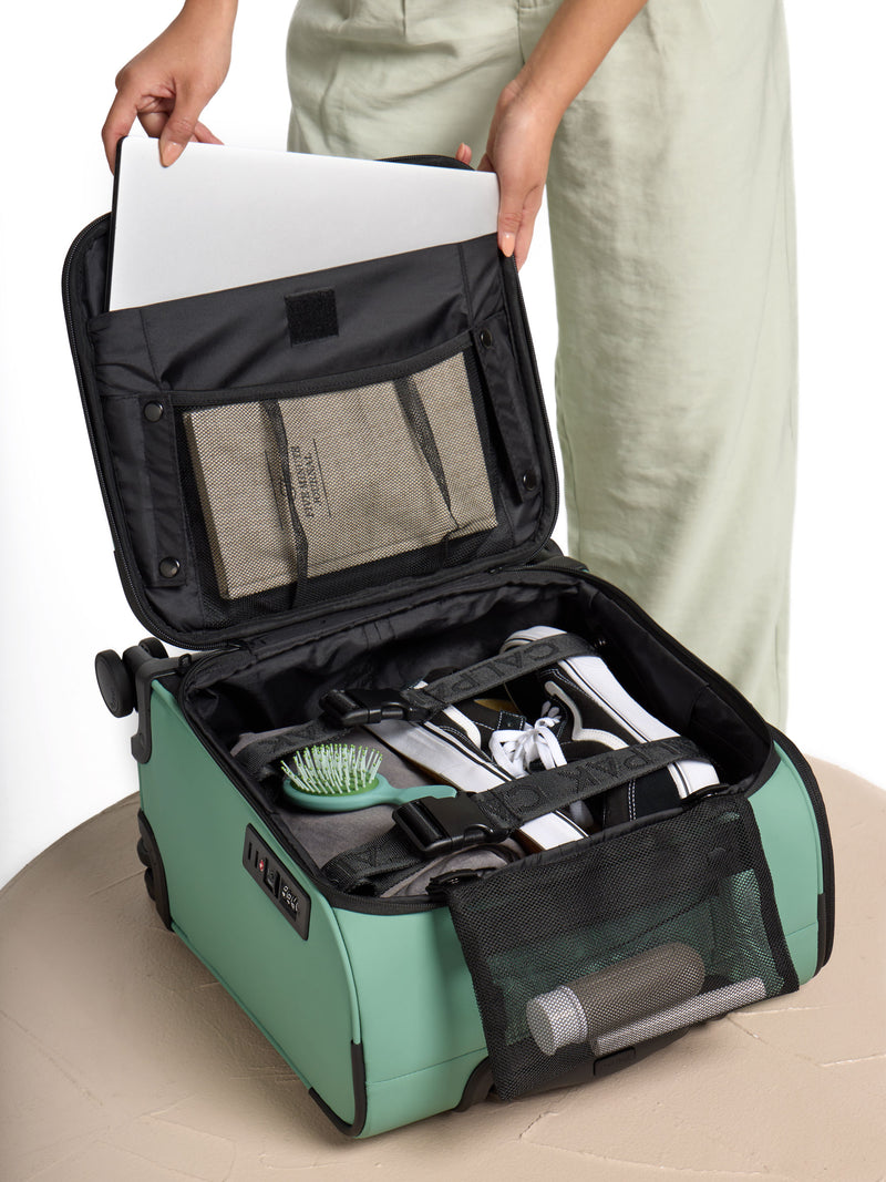 Model placing laptop and belongings inside the CALPAK Luka Mini Carry-On Luggage in green sage