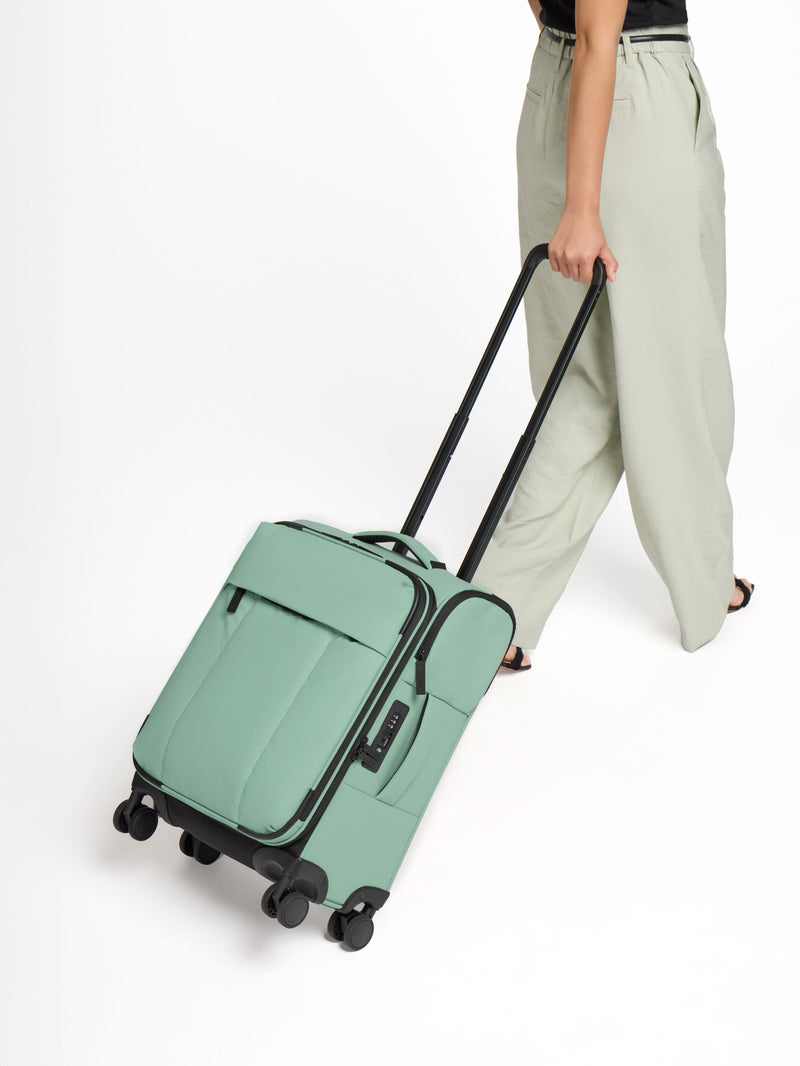 Model rolling CALPAK Luka Soft-Sided Carry-On Luggage in sage green