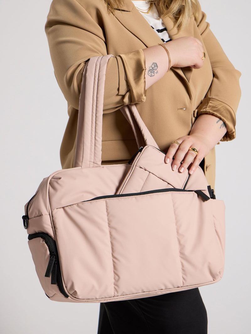 Model placing rose quartz CALPAK Luka Zippered Passport Wallet inside front pocket of Luka Duffel in rose quartz