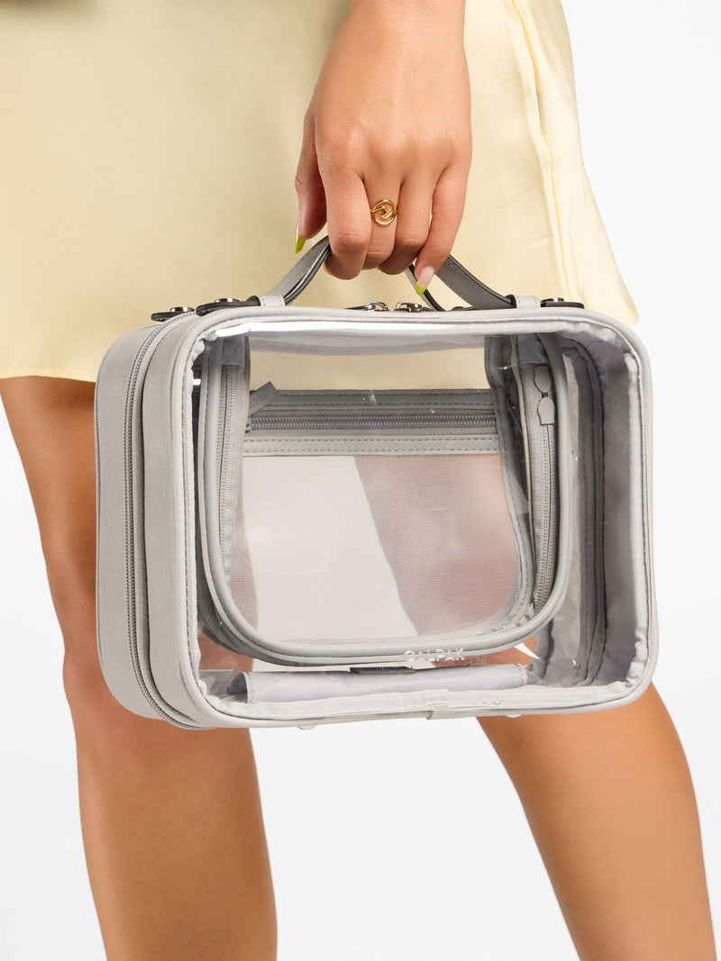 Model holding top handle of grey Medium Clear Cosmetics Case by CALPAK